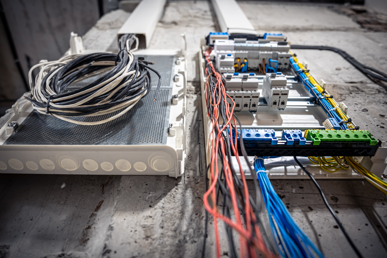 Conjunto de cables eléctricos organizados sobre una superficie de concreto, con un panel de distribución y terminales de conexión visibles. La imagen muestra cables de diferentes colores, incluyendo negro, blanco, rojo, azul y amarillo, utilizados para la instalación eléctrica.