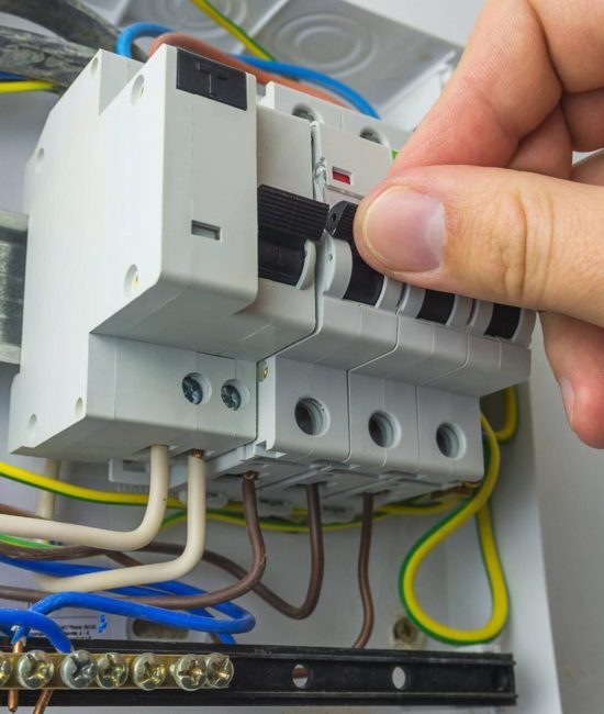 Mano ajustando un interruptor en un panel eléctrico con varios disyuntores y cables de colores, incluyendo azul, marrón y amarillo.
